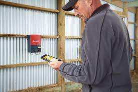 cattleman working the remote control of a SPEEDRITE 86000W elector fence charger on the wall inside a livestock barn
