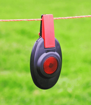 Patriot Fence Alert Black and red device attached to a fence wire with a green background