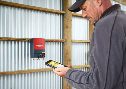 Cattle rancher working the remote control phone app of the Speedrite 46000W AC/Mains electric fence charger that is mounted on a barn wall.